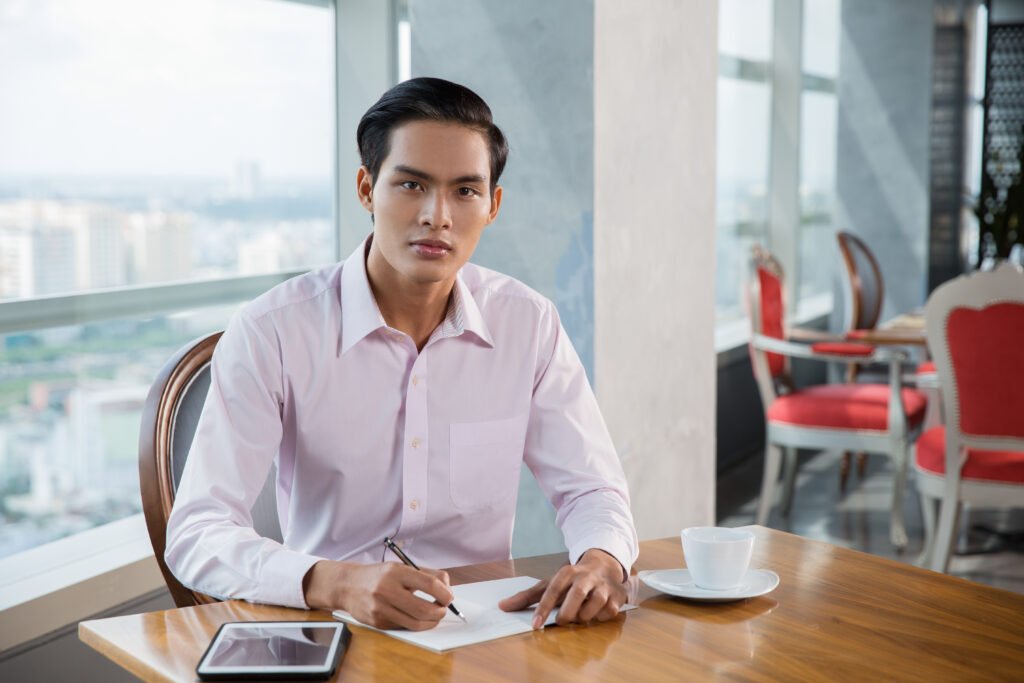 Serious Young Asian Man Writing in Cafe